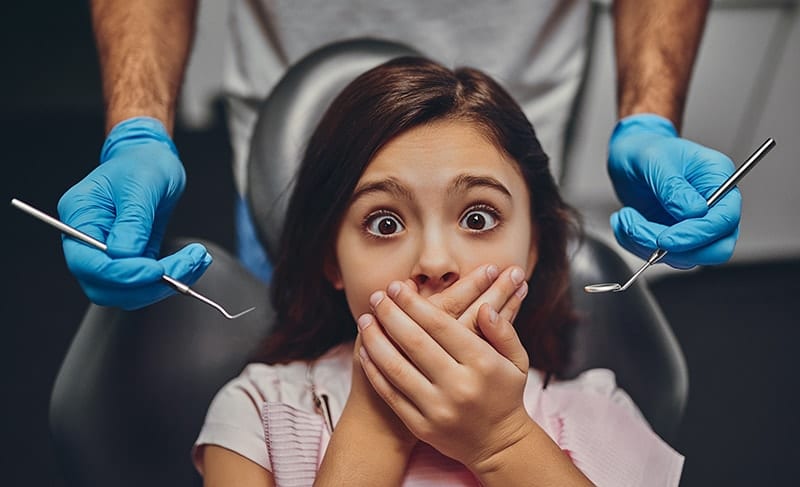 A young child covers her mouth in fear at the dentists office. It’s not surprising that as adults, we carry the fear and anxiety developed as children. The trauma is difficult to forget and, as most of us only visit the dentist once a year (and more than a third of us not even that!), easy to exaggerate in our minds. 